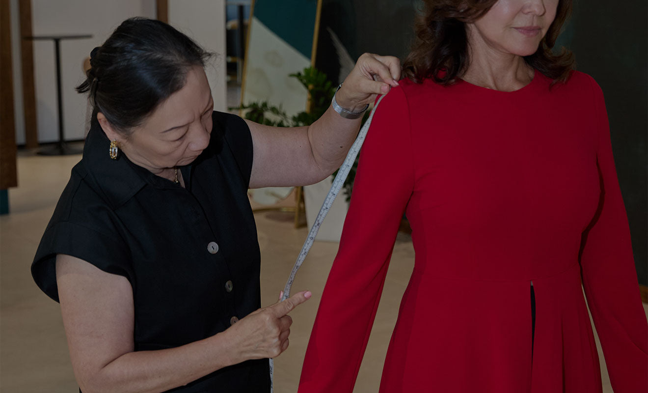 A designer pinning the waist of a red dress during a fit session