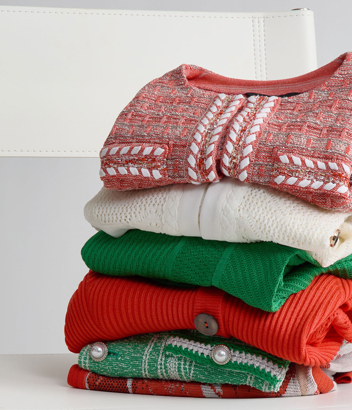 A stack of folded Misook silky-knit pieces in coral, ivory, green, and vermilion