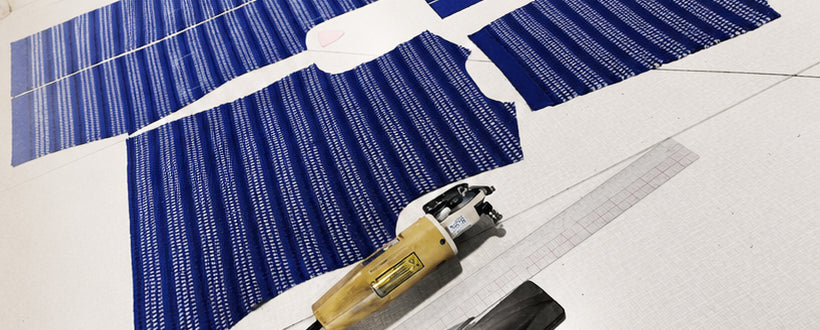 Cut panels of patterned blue knit laid out on the cutting table