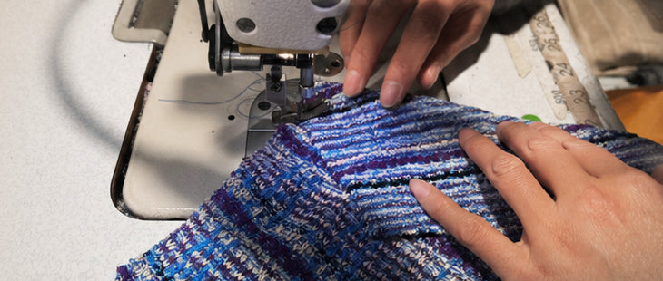 An operator guides panels of blue knit through the sewing machine