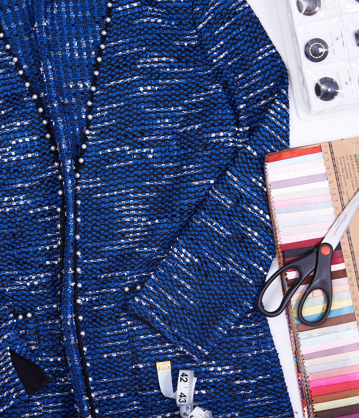 A finished cobalt tweed jacket laid out with its yarn swatches, buttons, and shears