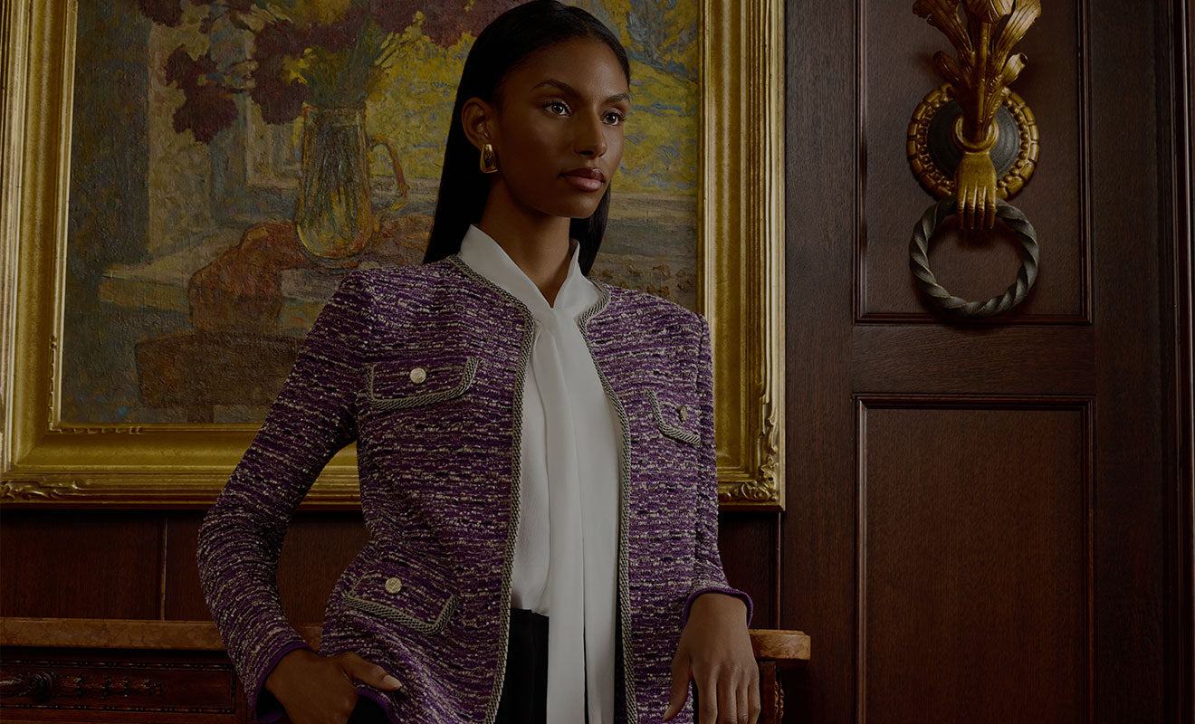 Campaign still — a model in a lilac tweed jacket against a panelled interior